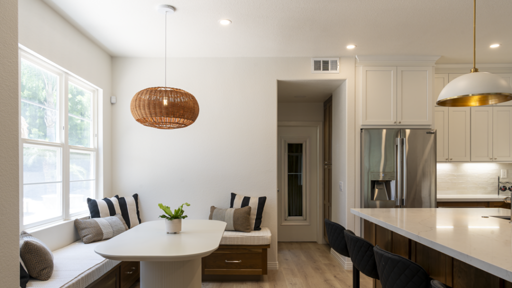 Window banquette with striped pillows, fluted pedestal table, woven rattan light, and glimpse of fridge