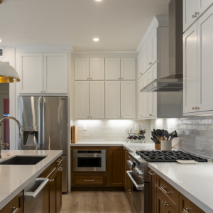 Cooking wall with stainless range and hood, stacked white cabinets, walnut lowers, and glossy subway-tile backsplash