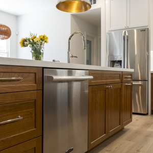Island dishwasher and faucet with brass-lined pendant above; French-door fridge and wood flooring in background
