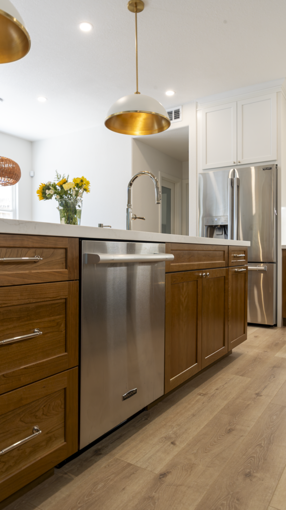 Island dishwasher and faucet with brass-lined pendant above; French-door fridge and wood flooring in background