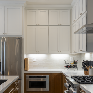 Close corner shot of fridge, microwave drawer, quartz counters, and two-tone cabinetry under under-cabinet lighting