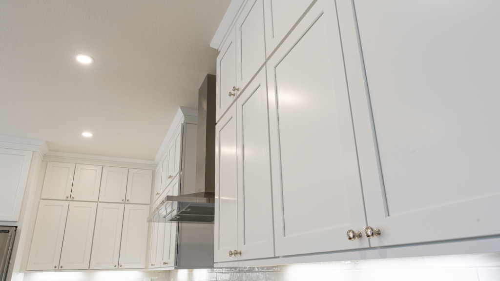 Upward angle of full-height stacked white shaker cabinets flanking stainless range hood and crown trim