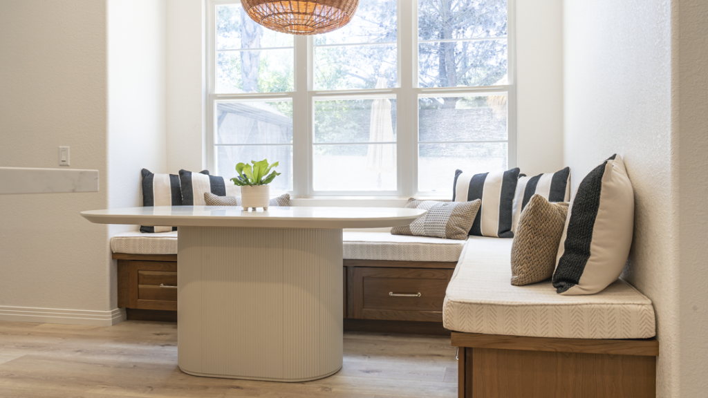 Front-on shot of storage banquette beneath triple window; neutral cushions and striped accent pillows