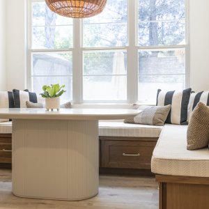 Front-on shot of storage banquette beneath triple window; neutral cushions and striped accent pillows