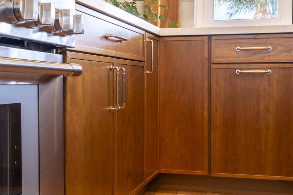 Cherry Amber base cabinetry at the range corner with polished pulls beneath quartz countertops