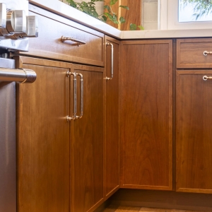 Cherry Amber base cabinetry at the range corner with polished pulls beneath quartz countertops