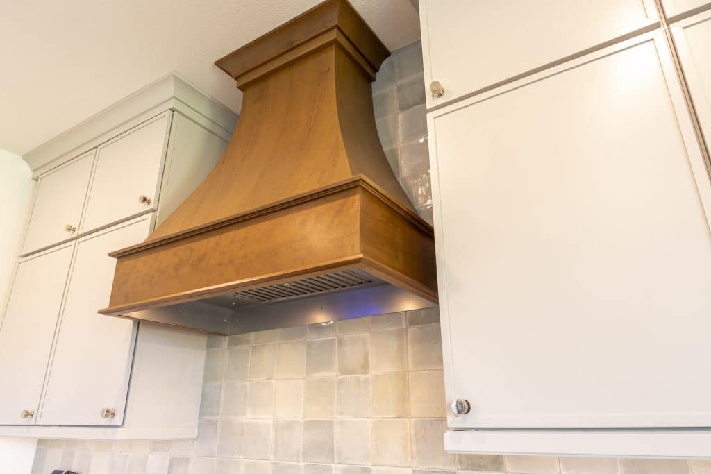 Detail of custom stained wood range hood framed by Painted Harbor uppers and handcrafted ceramic tile