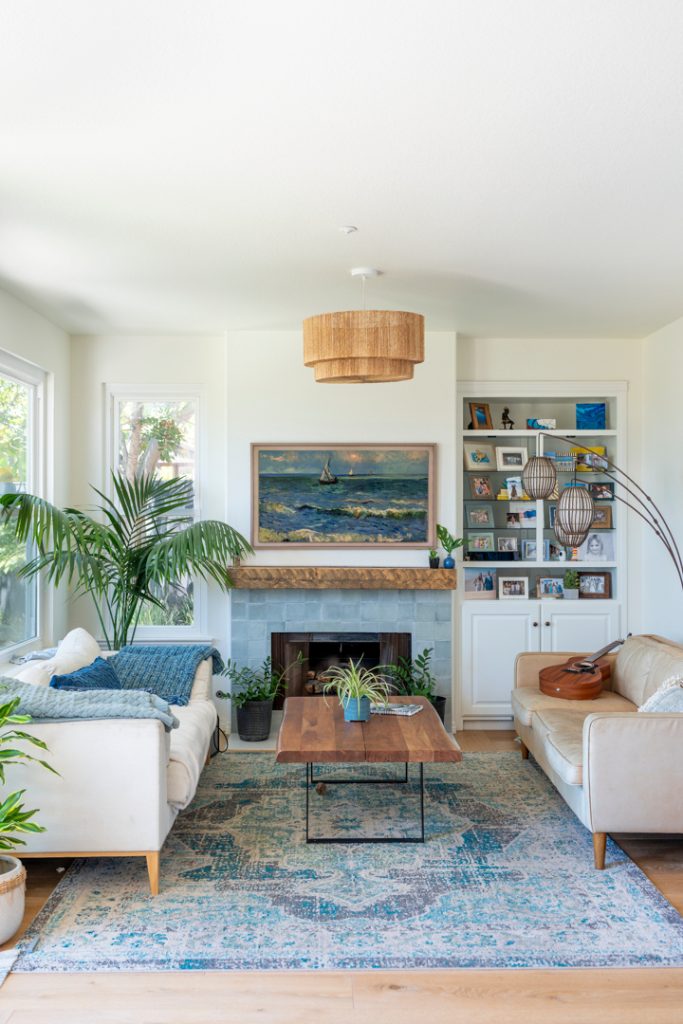 Adjacent family room with coastal fireplace surround, built-ins, woven pendant, and layered blue accents