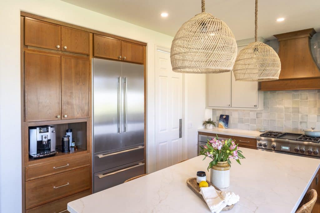 Built-in French-door refrigerator and coffee niche beside island with quartz top and woven pendants in a warm cherry and paint palette