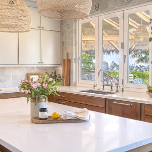Quartz island vignette looking to sink wall&mdash;woven pendants, Painted Harbor uppers, Cherry Amber lowers, and full-height ceramic backsplash