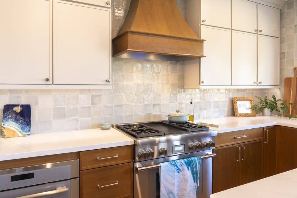 Thermador ProHarmony gas range beneath custom wood hood with glossy Marin ceramic tile and two-tone cabinetry