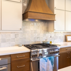 Thermador ProHarmony gas range beneath custom wood hood with glossy Marin ceramic tile and two-tone cabinetry