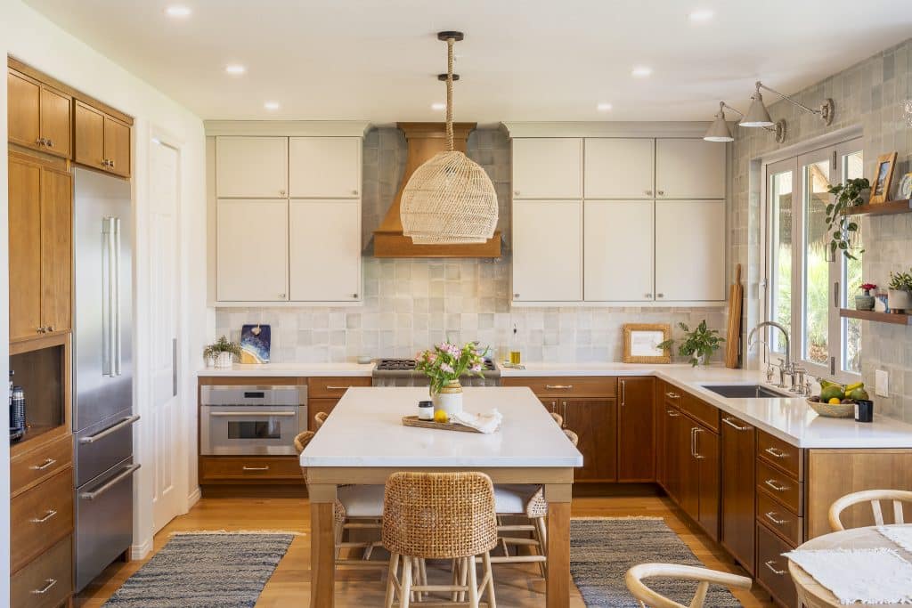 Centered view of two-tone kitchen with large island seating, custom wood hood, zellige-style Marin tile backsplash, and soft recessed lighting
