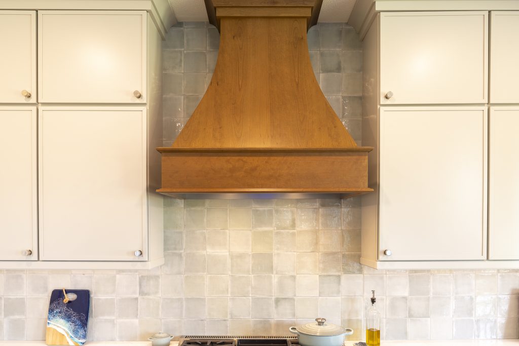 Centered view of custom stained wood hood with glossy Marin ceramic tile backsplash and Painted Harbor uppers