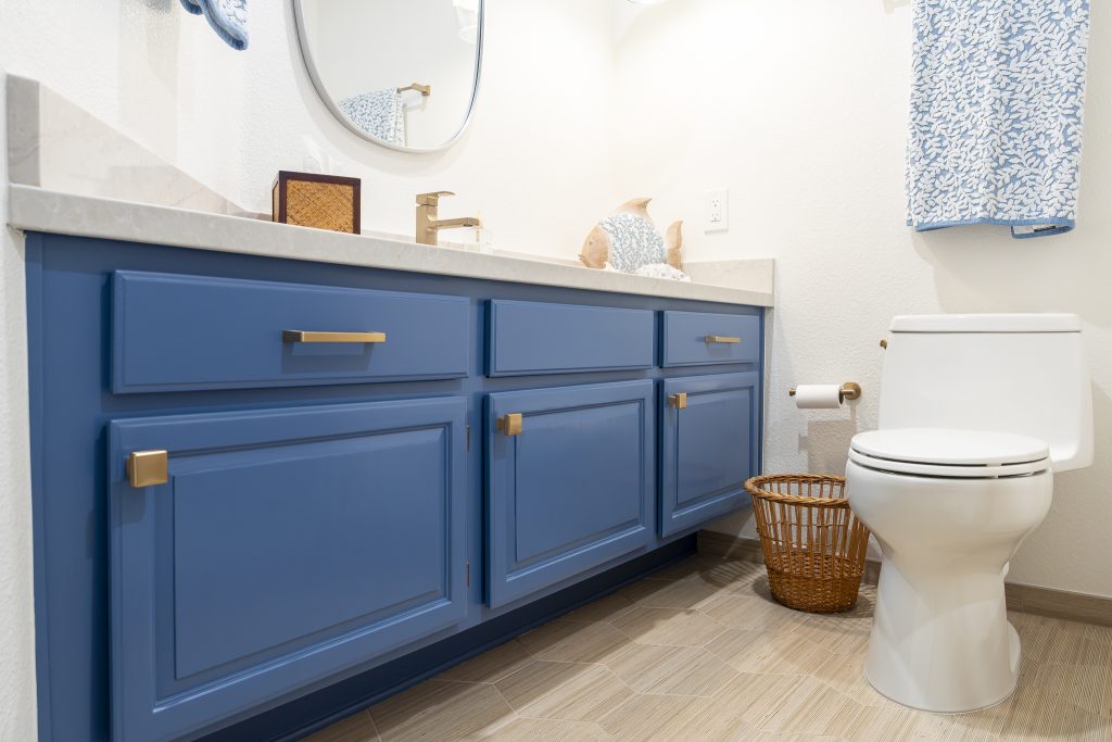 Blue cabinet vanity with brass pulls beside the toilet; light quartz countertop
