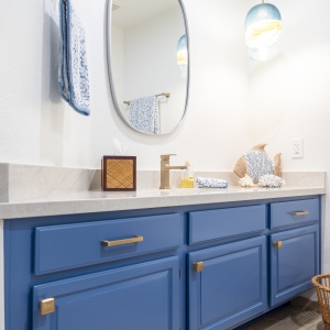 Blue vanity with brass hardware and MSI Lumat&aacute;j quartz under an oval mirror and pendant.