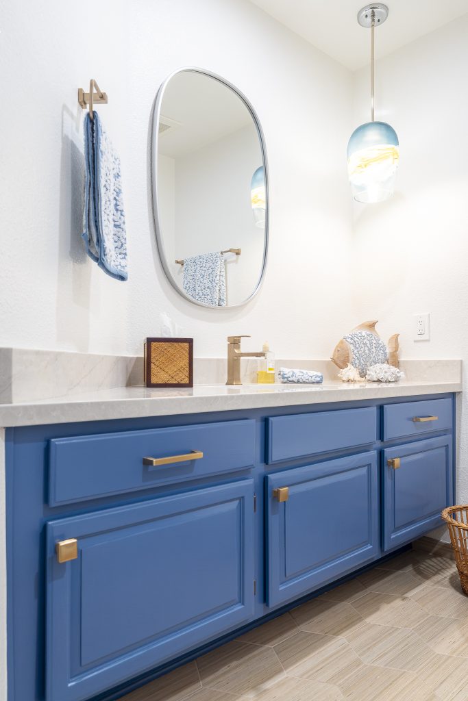 Blue vanity with brass hardware and MSI Lumatáj quartz under an oval mirror and pendant.
