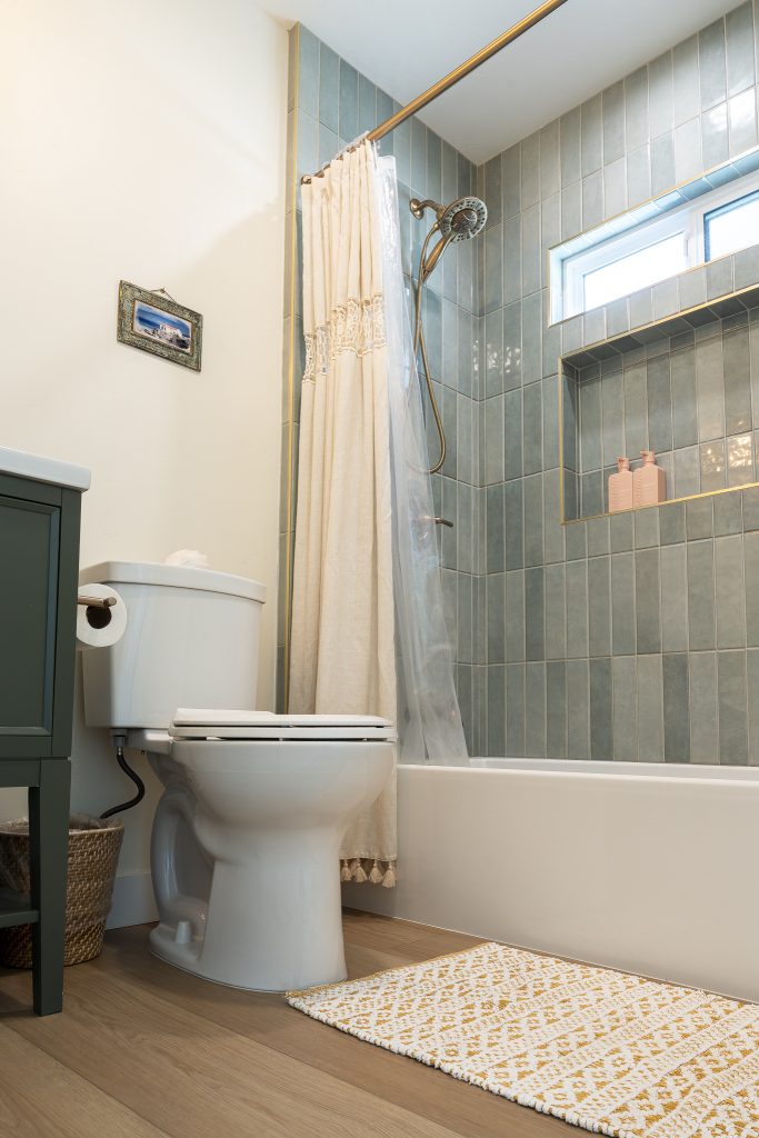 Guest bath tub&ndash;shower with vertical sea-green tile and niche
