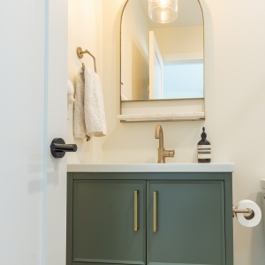 Guest bath vanity in green with brass sconce and arched mirror
