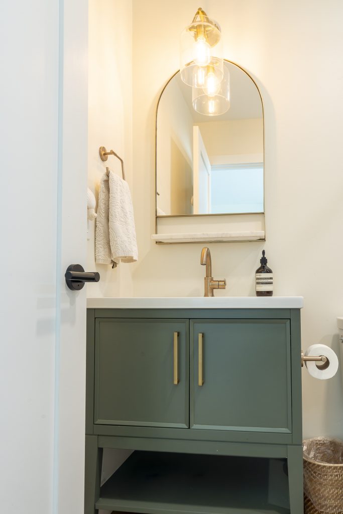 Guest bath vanity in green with brass sconce and arched mirror