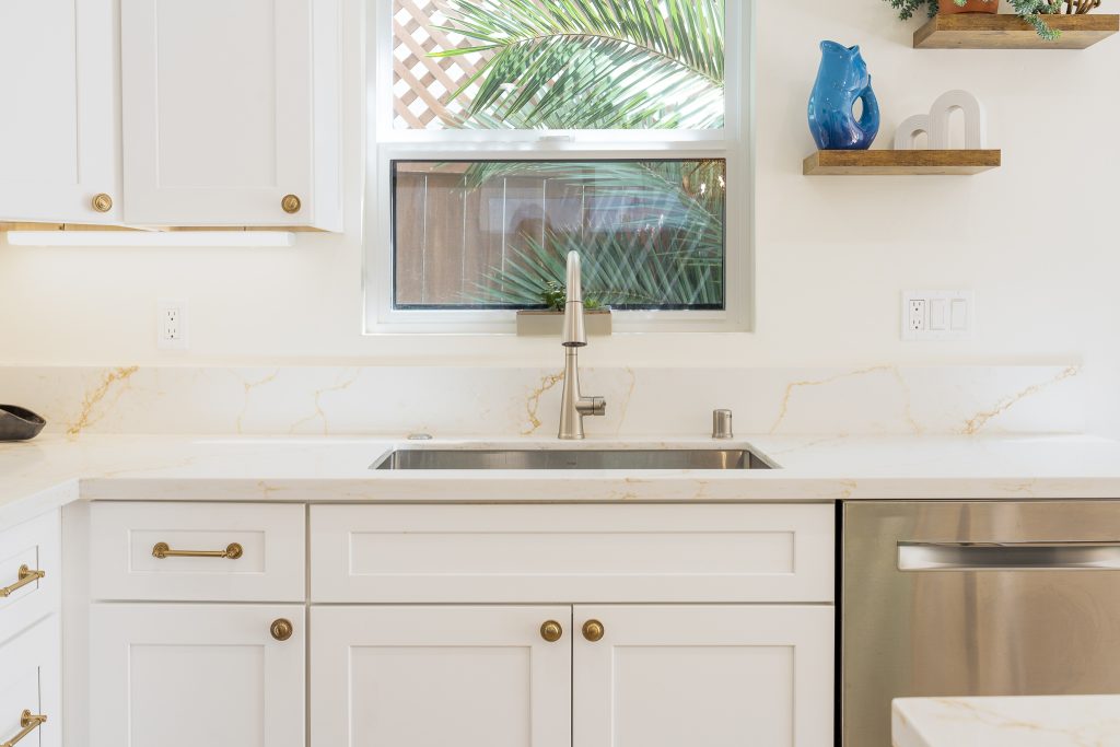 Undermount sink at window with floating shelves and quartz backsplash