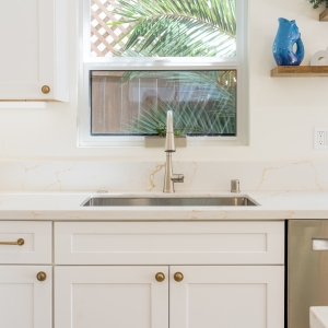 Undermount sink at window with floating shelves and quartz backsplash