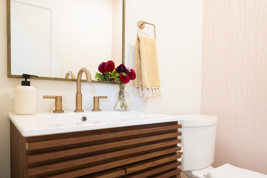 Powder bath vanity with brass faucet and soft patterned wallpaper