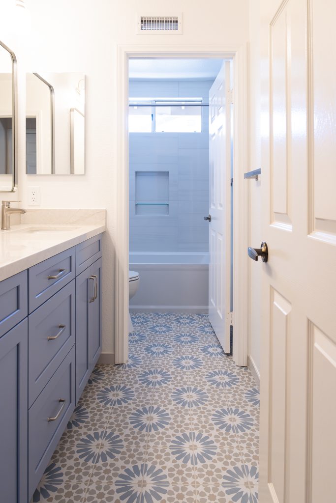 Patterned Ethnic porcelain floor with blue vanity leading to a Kohler Archer tub surround