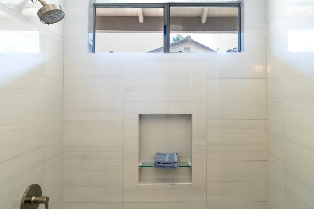 Shower niche with glass shelf centered below a high window in Bianco Lasa wall tile