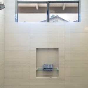 Shower niche with glass shelf centered below a high window in Bianco Lasa wall tile