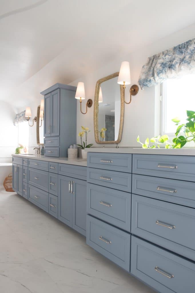 Long blue double-sink vanity with gold sconces, woven-frame mirrors, and quartz countertop