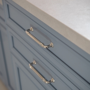 Close-up of quartz countertop edge and polished nickel cabinet pulls on blue vanity drawers