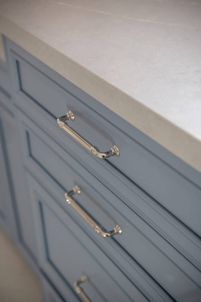 Close-up of quartz countertop edge and polished nickel cabinet pulls on blue vanity drawers