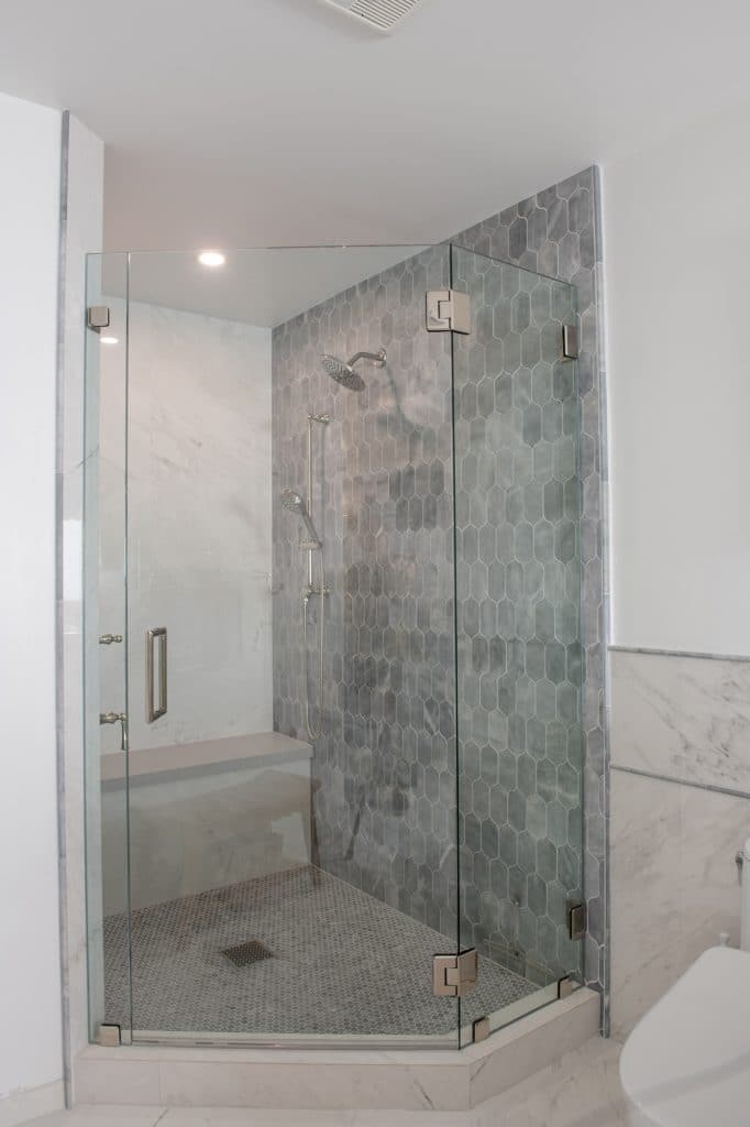 Corner shower with frameless glass panels, blue-gray lotus tile wall, and penny round shower floor