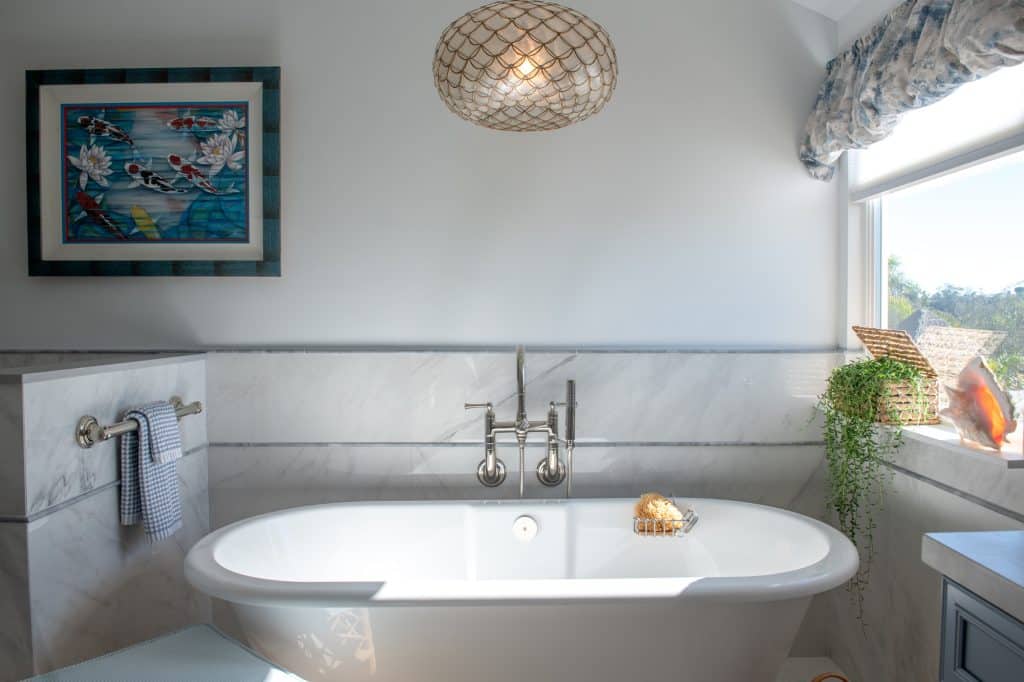 Freestanding soaking tub with marble-look wainscot wall and pendant light in primary bathroom