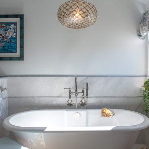 Freestanding soaking tub with marble-look wainscot wall and pendant light in primary bathroom