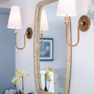 Gold wall sconce beside woven-frame mirror above bathroom vanity