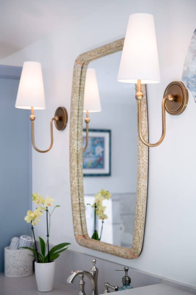 Gold wall sconce beside woven-frame mirror above bathroom vanity