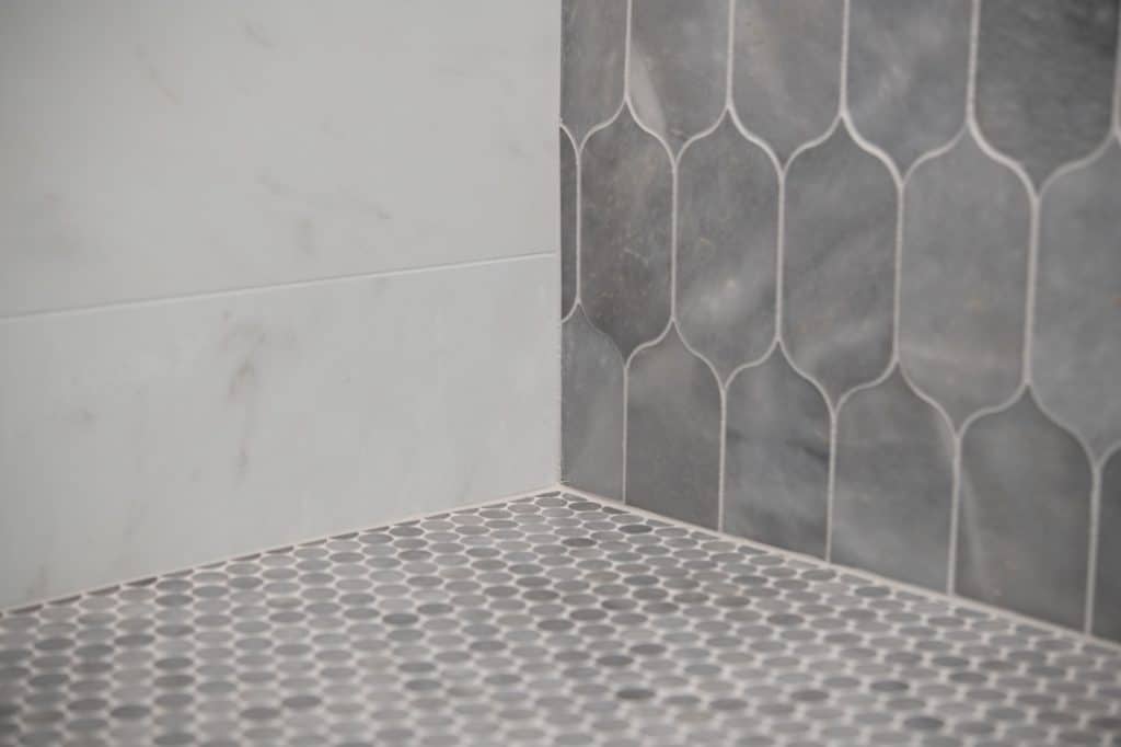 Penny round mosaic shower floor detail with marble-look wall tile and lotus accent tile