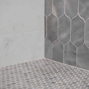 Penny round mosaic shower floor detail with marble-look wall tile and lotus accent tile