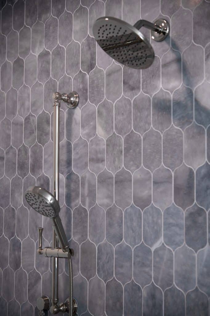Chrome rain shower head and handheld sprayer on blue-gray lotus tile shower wall