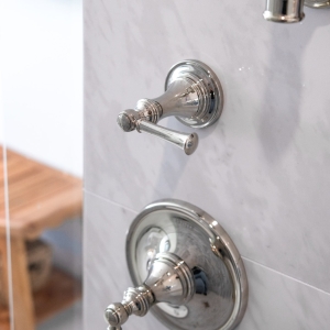 Chrome shower valve and trim detail mounted on marble-look tile wall