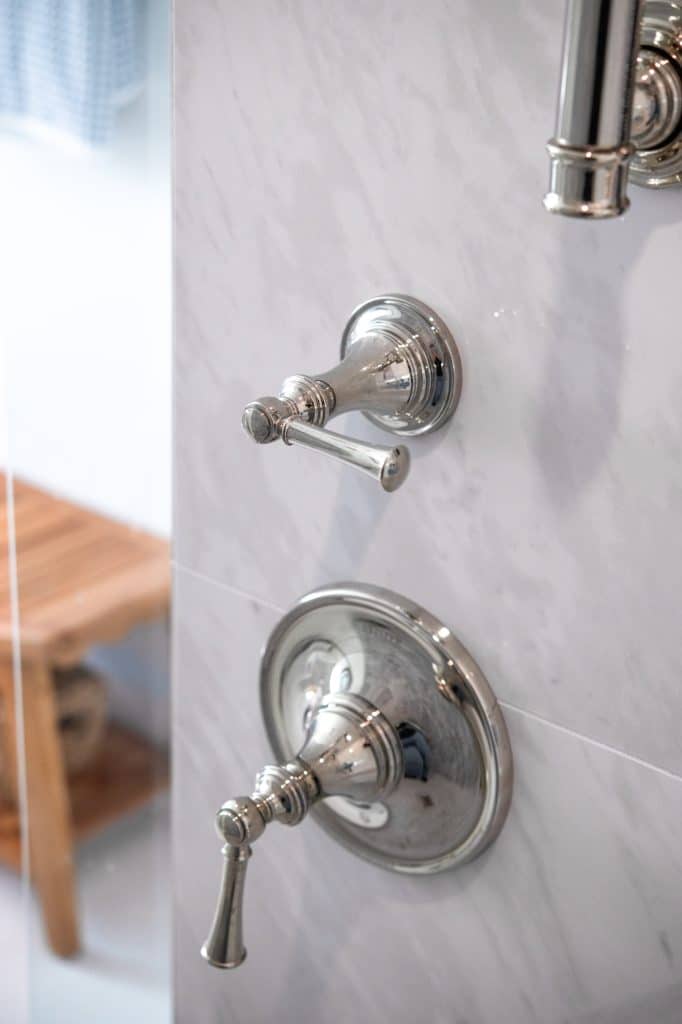 Chrome shower valve and trim detail mounted on marble-look tile wall