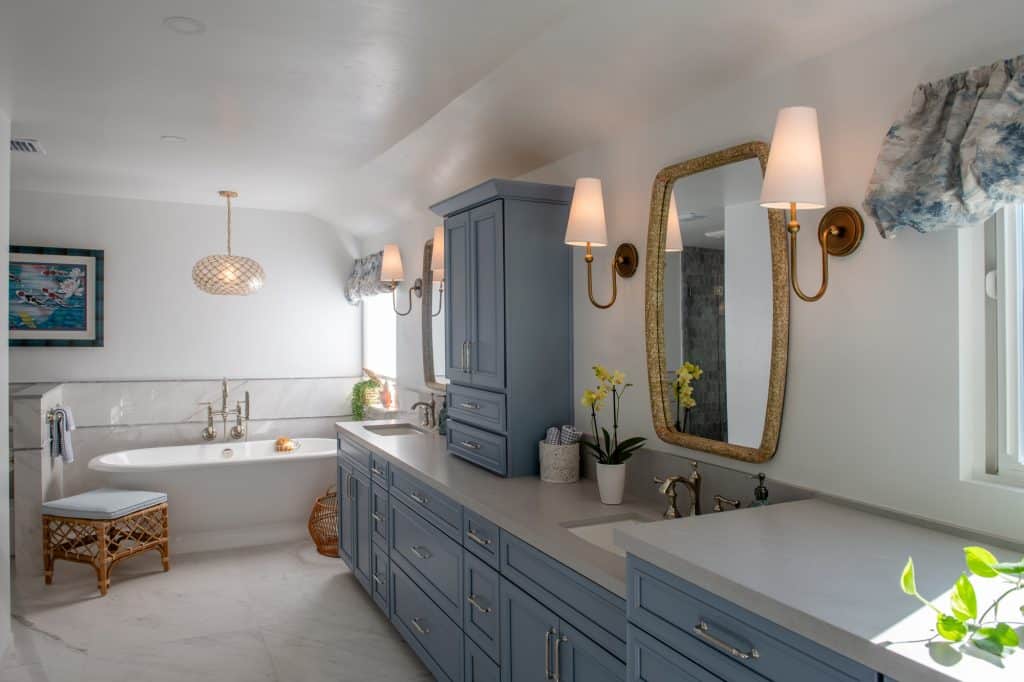 Primary bath perspective showing blue vanity, pendant lighting, and soaking tub with tile wainscoting