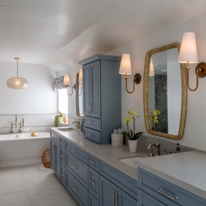 Primary bath perspective showing blue vanity, pendant lighting, and soaking tub with tile wainscoting