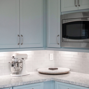 Corner countertop with small appliance storage beneath blue cabinets and built-in microwave