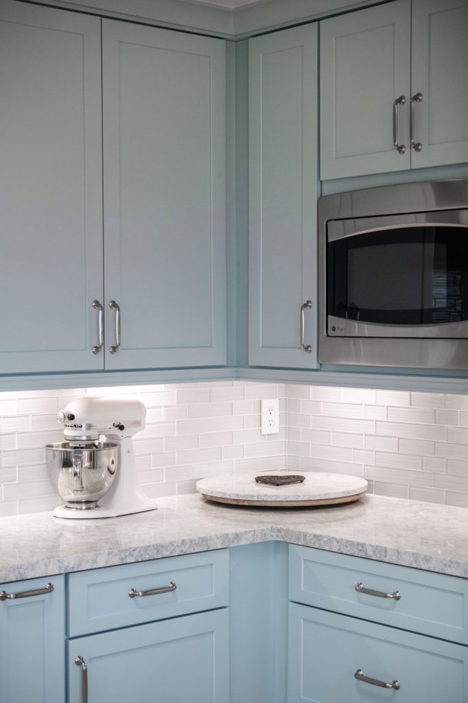 Corner countertop with small appliance storage beneath blue cabinets and built-in microwave