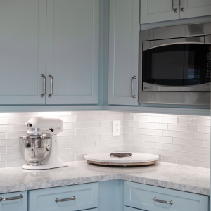 Corner kitchen counter view with mosaic backsplash, quartz surface, and custom blue cabinetry