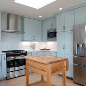 Angled view of remodeled kitchen with blue cabinets, skylight, stainless refrigerator, and butcher-block prep cart