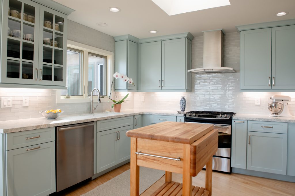 Kitchen view showing blue cabinetry, window over sink, glass-front uppers, and stainless range and hood